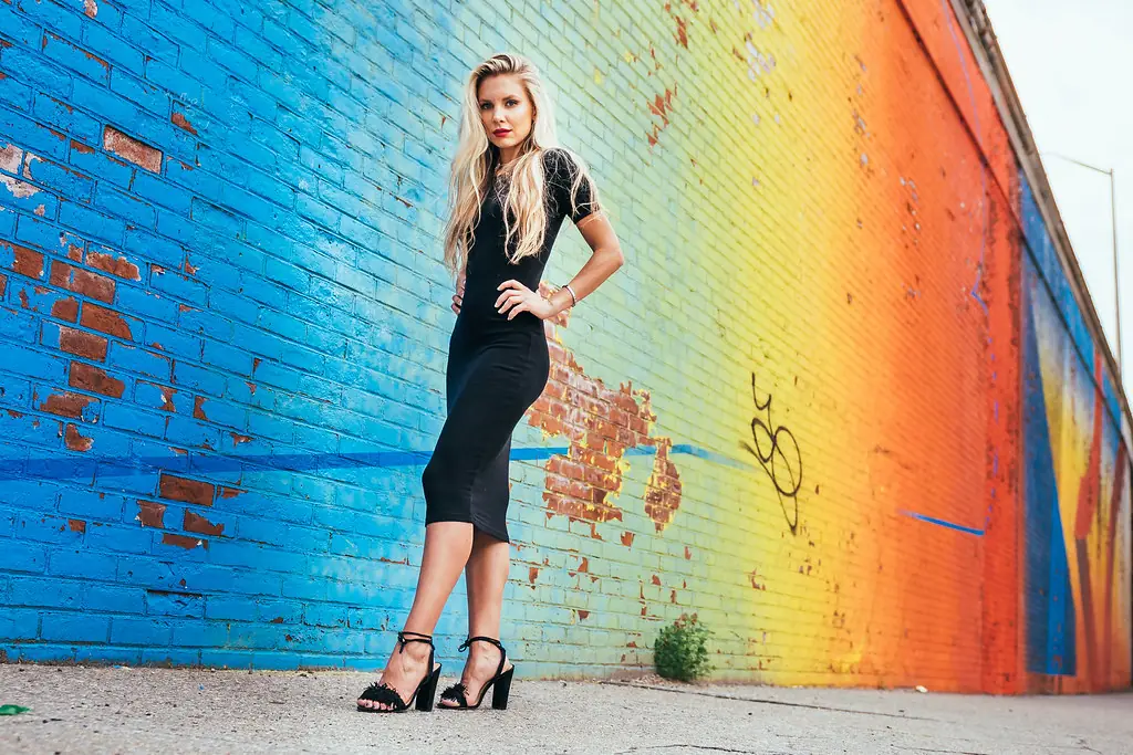 Woman in a black dress against a rainbow-painted brick wall