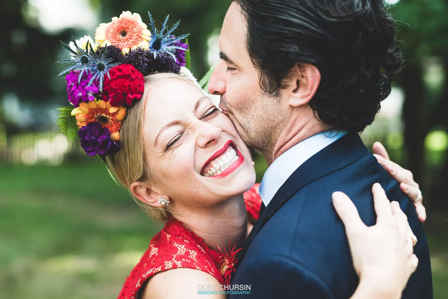 Bride in a flower crown laughing as the groom kisses her cheek